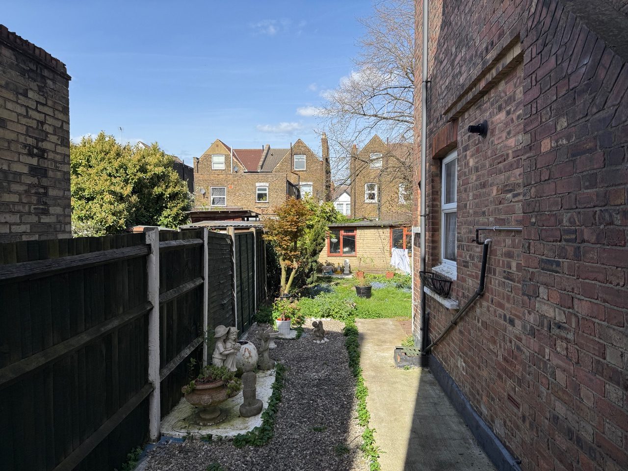 Narrow side passage at [REDACTED] between the fence and the side wall of the house, illustrating the tunnel-like enclosure effect
