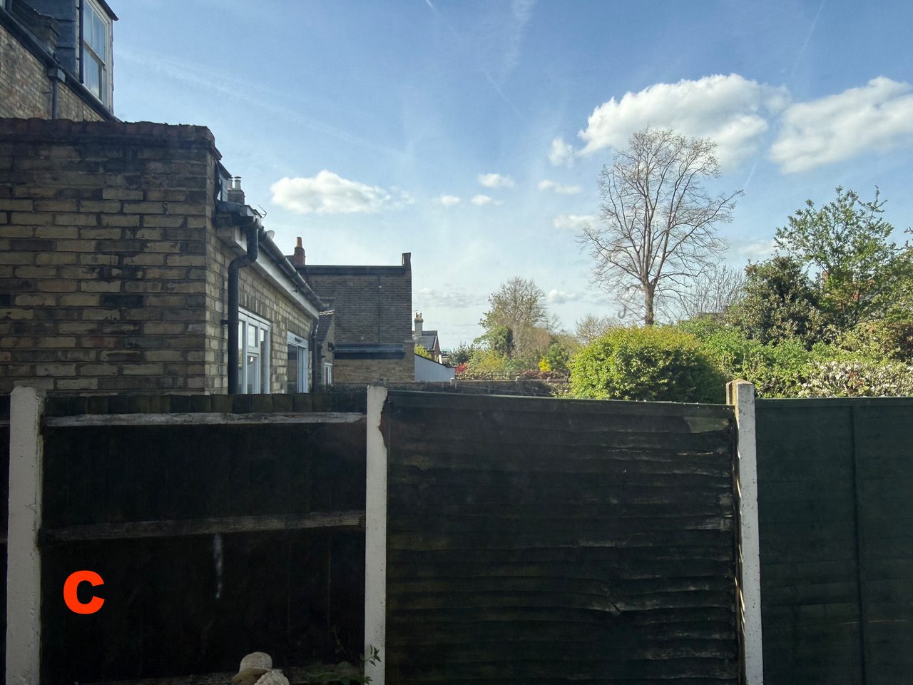 View out of window C at [REDACTED], showing open sky and trees above the fence line