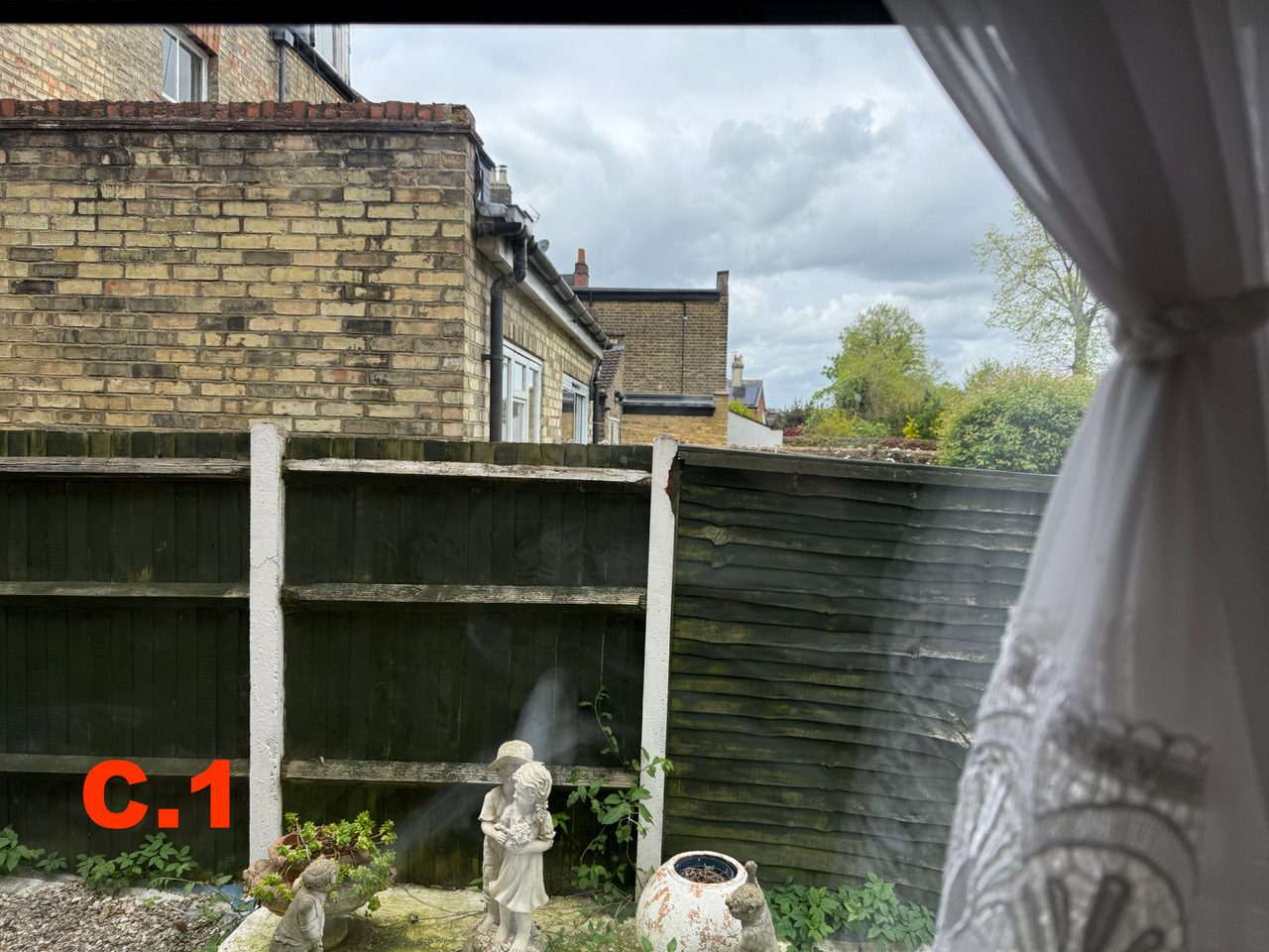 Second view from window C at [REDACTED], showing rooftops and sky over the boundary fence
